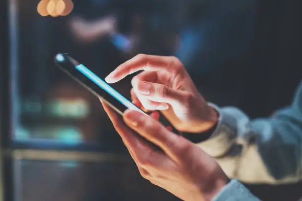 Photo of Closeup view of woman holding modern smartphone in hands.Girl typing on empty mobile screen. Horizontal, blurred background, bokeh effects.