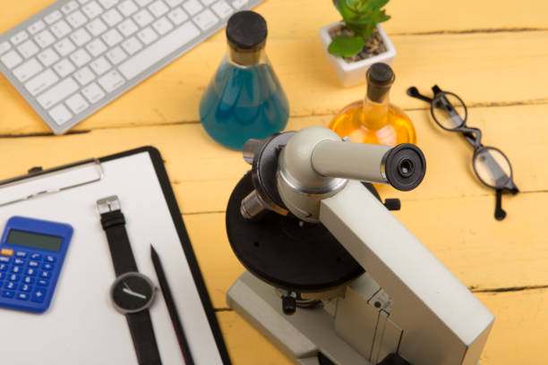 istock Education and science concept - microscope, book, magnifying glass, calculator, watch, blank clipboard, computer keyboard, eyeglasses and chemical liquids 869411868