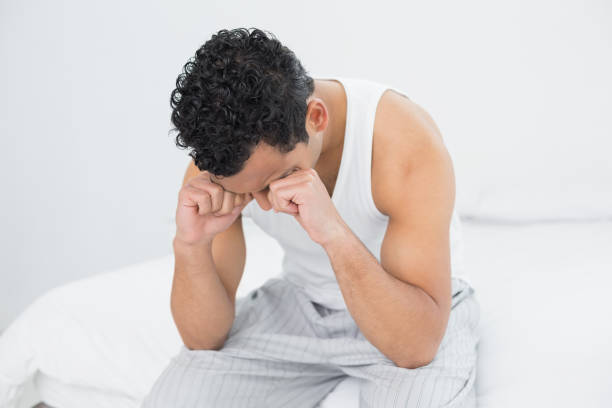 istock Young sleepy man rubbing his eyes on bed 869415968