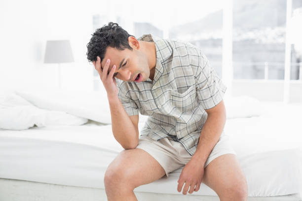 istock Man sitting and yawning in bed 869416170