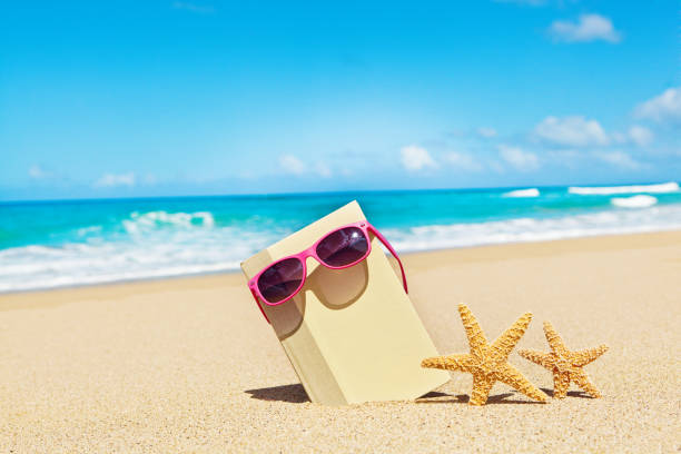 A hard cover book wearing sunglasses with couple of starfish on a tropical beach. Concept for Summer reading.