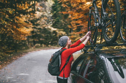 Young woman taking bikes from the car roofrack to start a cycling adventure through the colorful autumn forest