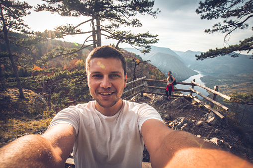 Young man taking a selfie on top of the cliff with his female friend and a beautiful landscape view of the lake perucac behind him