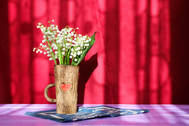 bouquet de fleurs de lys-de-la-vallée dans une tasse en céramique avec un cœur sur une serviette bleu et violet table sur fond bordeaux - claret cup photos et images de collection