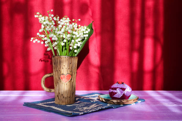 bouquet de fleurs de lys-de-la-vallée dans une tasse en céramique avec un cœur sur une serviette bleu et violet table sur fond bordeaux - claret cup photos et images de collection