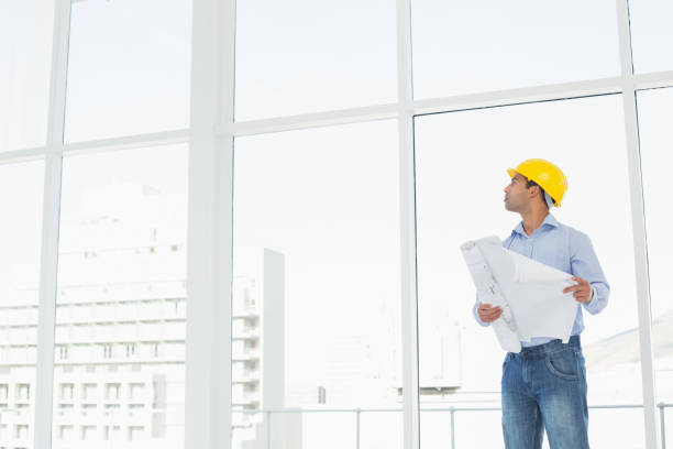 istock Architect in yellow hard hat with plans looking up at window 869433788