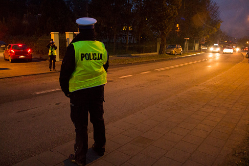 Poland, Gdansk, 1st November 2017 - Police directing traffic at night. Policeman wearing police uniform and yellow orange reflective vest. His looking at cars on the street.