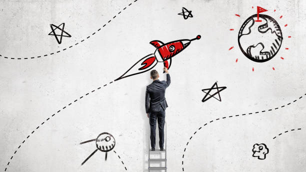 A businessman draws paints a rocket that will reach a goal set on a planet's surface.