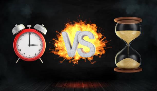 istock 3d rendering a large flaming word VS stands between a red retro alarm clock and a hourglass. 869440790