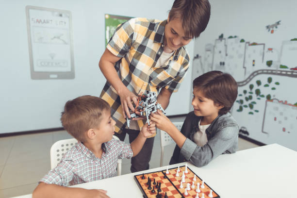 istock The guy brought two bored boys a gray robot. Next to them stands a chessboard with chess pieces 869452934