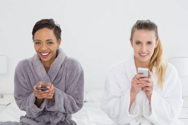 istock Female friends in bathrobes text messaging on bed 869455782