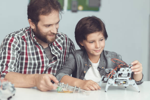 istock A man helps a boy with a robot assembly. A man watches as the boy finishes assembling the robot 869456546