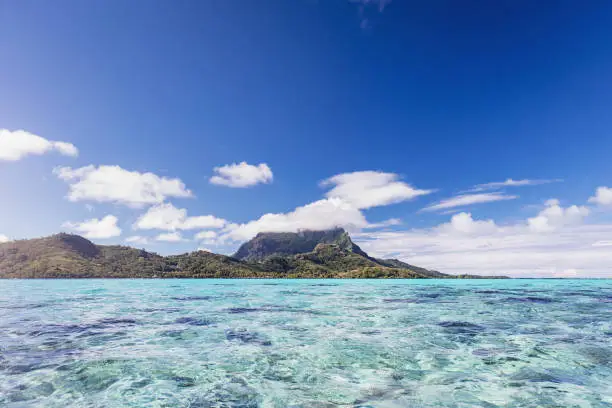 Turquoise clear lagoon of Bora Bora Island. Cumulus cloud covering the famous peak of Mount Otemanu. Bora Bora Island, Society Islands, French Polynesia
