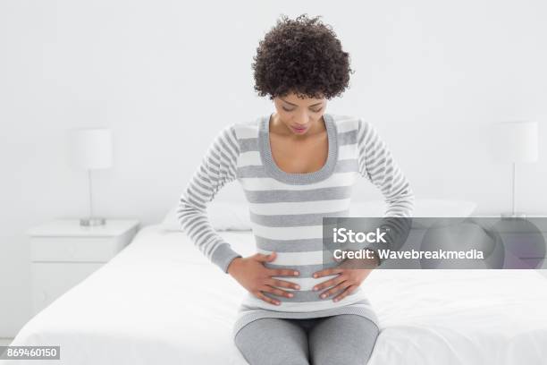 Lässige Frau Mit Magenschmerzen Im Bett Sitzen Stockfoto und mehr Bilder von Hand am Bauch - Hand am Bauch, Frauen, Junge Frauen