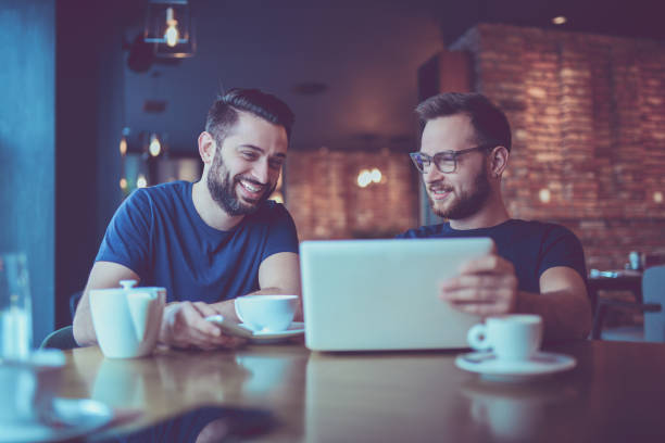 istock Two Smiling  Male Freelancers Drinking Coffee and Video Conferencing In Cafe Restaurant 869465972
