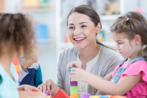 istock Beautiful young kindergarten teacher sits with students at school 869476044
