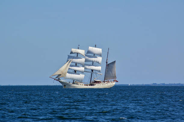 istock Square-rigged white sailing ship at sea with a distant shore in the far background 869503024