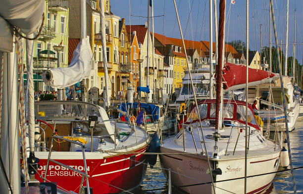 Sonderborg, Denmark - July 5th, 2012 - Sailing yachts at their moorings in the Sonderborg city harbor with colorful waterfront facades lit by the evening sun in the background stock photo