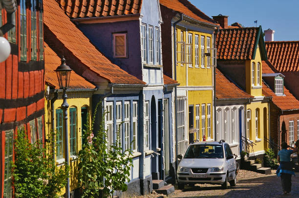 Aeroskobing, Denmark - July 4th, 2012 - Narrow cobblestone street on the island of Aero with colorful historic residential buildings, parked car, pedestrian stock photo