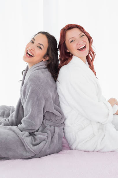 istock Cheerful friends in bathrobes sitting back-to-back on bed 869507076