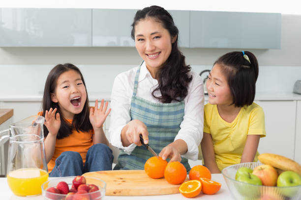 istock Woman with cheerful two daughters cutting fruit in kitchen 869517434