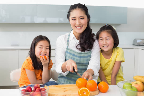 istock Woman with happy two daughters cutting fruit in kitchen 869517438