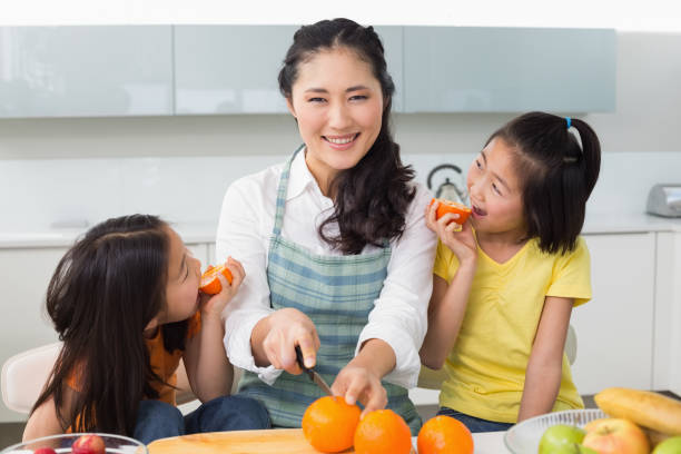 istock Woman with happy two daughters cutting fruit in kitchen 869517442