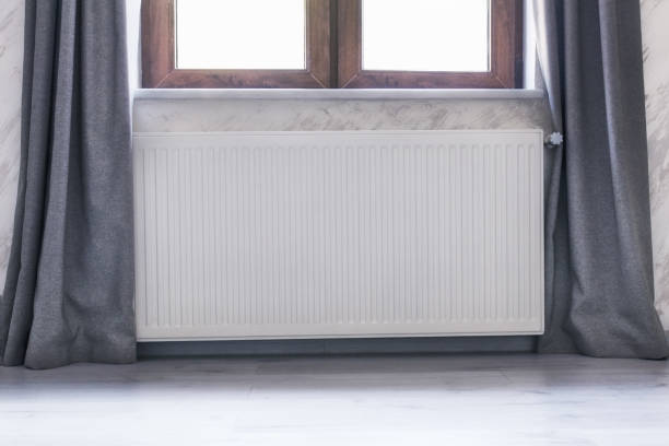 istock Heating radiator under the window with a wooden frame and curtains. 869520336
