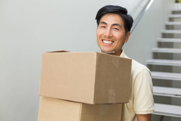 istock Smiling young man carrying boxes against staircase 869524158