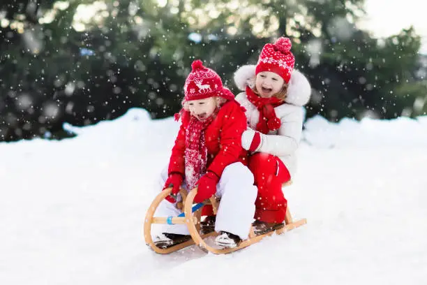 Little girl and boy enjoy a sleigh ride. Child sledding. Toddler kid riding a sledge. Children play outdoors in snow. Kids sled in Alps mountains in winter. Outdoor fun for family Christmas vacation.