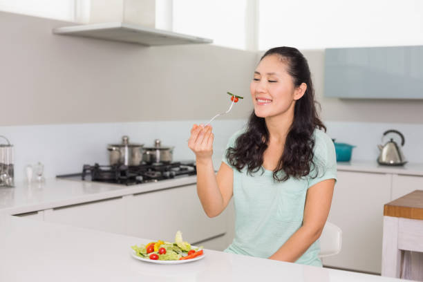 istock Happy young woman eating salad in kitchen 869527214