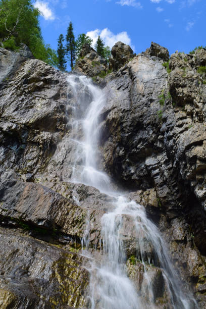 istock Shirlak waterfall in rocks on blue sky with white clouds background. Tektu river, Altai Mountains, Altay Republic, Siberia, Russia. Vertical orientation 869541134