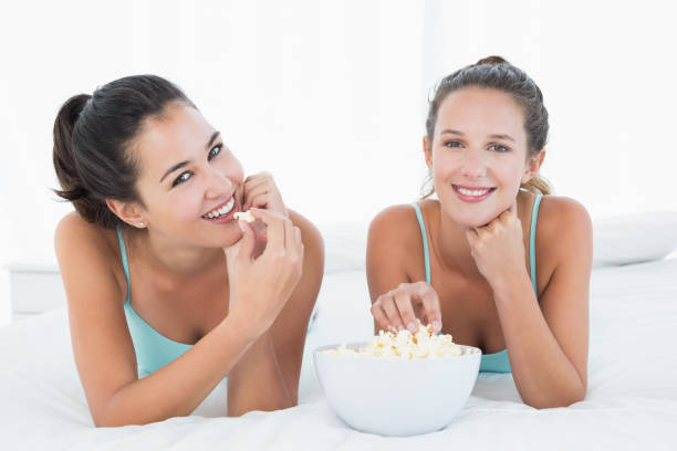 istock Smiling female friends eating popcorn in bed 869545192