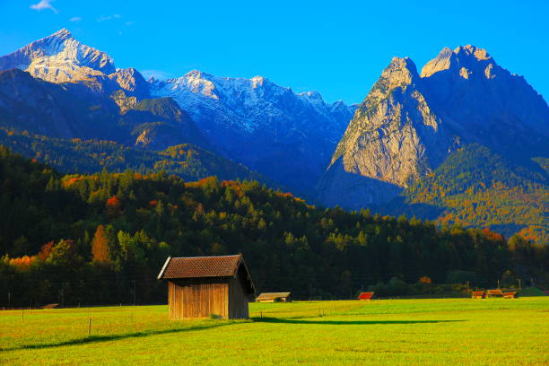 istock Alpine Rustic wooden barn farm, with Zugspitze, Waxenstein and Alpspitze view– dramatic landscape in Bavarian alps, Germany, near Karwendel mountain range - Majestic alpine landscape in autumn – Garmisch, Bavaria, Germany 869551642