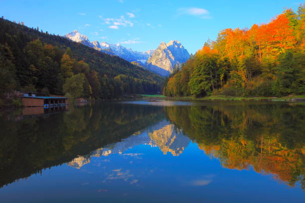 Riessersee alpine turquoise lake with reflection at gold colored sunrise, with Zugspitze, Waxenstein and Alpspitze view– dramatic landscape in Bavarian alps, Germany - Majestic alpine landscape in autumn, Snowcapped mountains – Garmisch, Bavaria, Germany lago alpino de turquesa riessersee, con reflejo al amanecer color oro, con el zugspitze, waxenstein y alpspitze vista espectacular paisaje en los alpes bávaros, alemania - majestuoso paisaje alpino en las montañas nevadas, otoño – garmisch, baviera, alemania