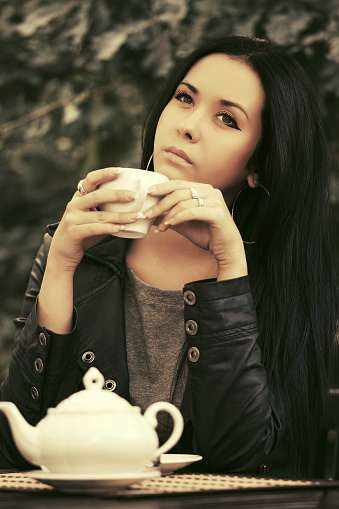 Young fashion woman in leather jacket drinking a tea at sidewalk cafe