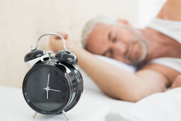 istock Man sleeping in bed with alarm clock in foreground 869560728