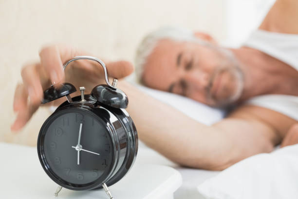istock Mature man extending hand to alarm clock in bed 869560738