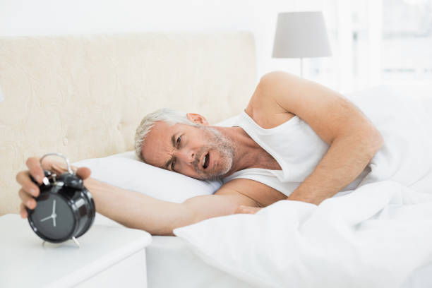 istock Mature man extending hand to alarm clock in bed 869560746