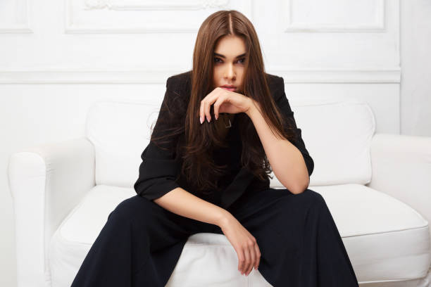 Young fashion woman in black jacket sitting on sofa at home stock photo