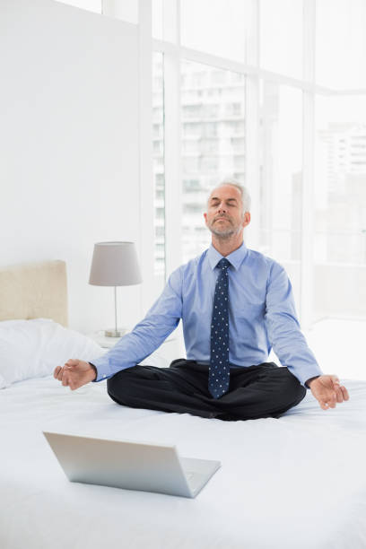 istock Businessman sitting in lotus pose with laptop on bed 869564298