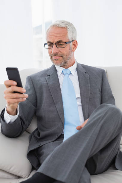 istock Elegant mature businessman text messaging on sofa 869569498