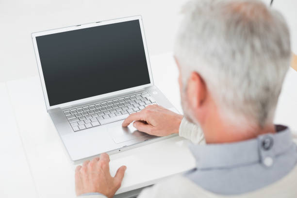 istock Closeup rear view of a grey haired man using laptop at desk 869570476