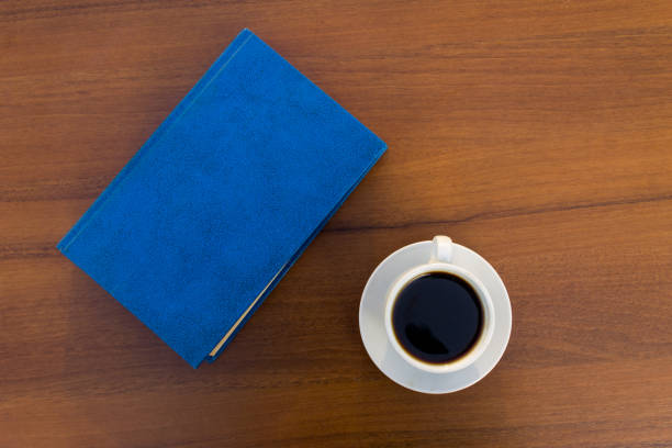 Cup of coffee and closed book on wooden table. Top view