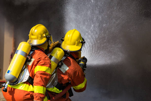 two firefighters water spray by high pressure nozzle surround with dark smoke stock photo