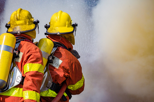 two firefighters water spray by high pressure nozzle surround with dark smoke and copy space