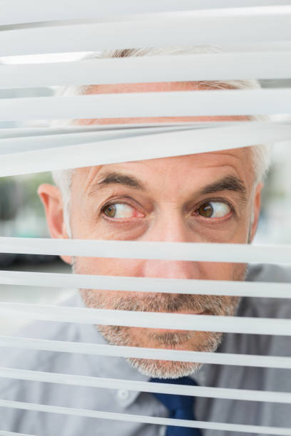 istock Closeup of a businessman peeking through blinds 869571236
