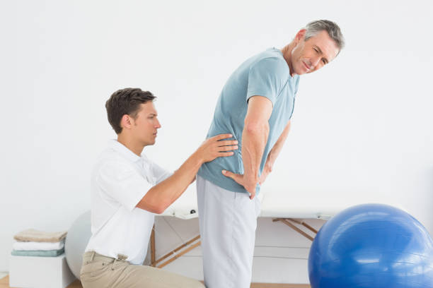 istock Therapist massaging mans lower back in gym hospital 869578116