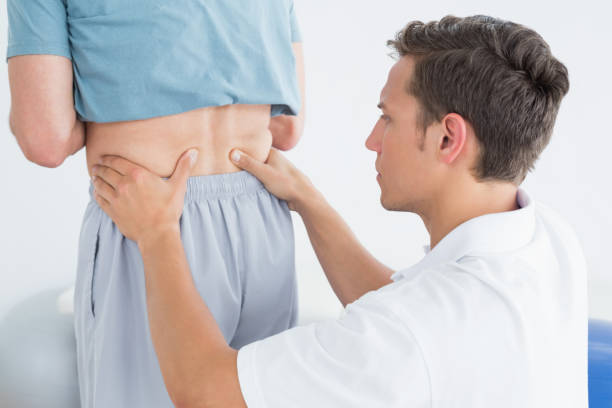 istock Hands massaging mans lower back in gym hospital 869578148