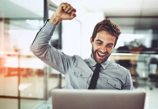 Shot of a handsome young businessman doing a fist pump while working on a laptop in an office